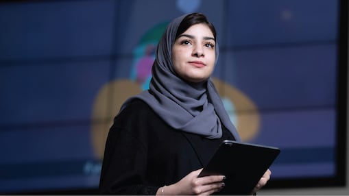 A person wearing a grey headscarf and black clothing is holding a tablet