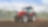  A red tractor ploughing a muddy field with trees in the background