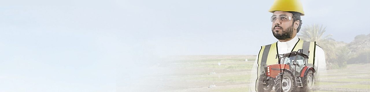 Man reading a document with a background of fields and a red tractor