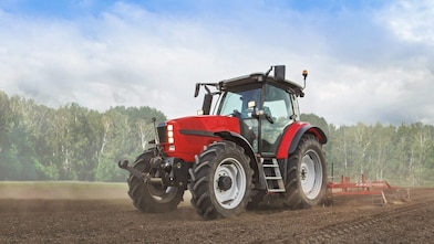 A red tractor ploughing a muddy field with trees in the background