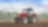 A red tractor ploughing a muddy field with trees in the background